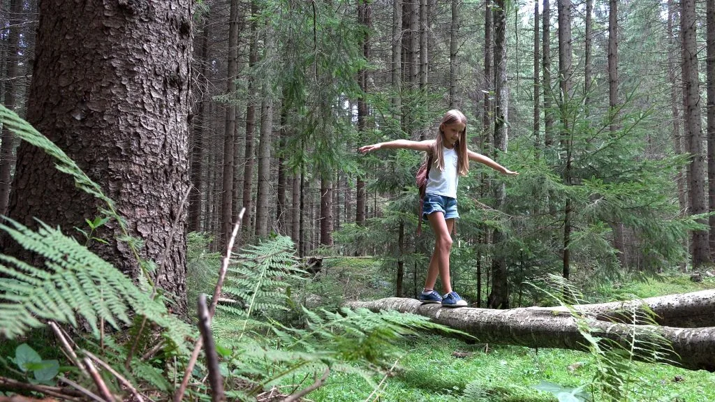 A teenage girl walks across a log in the forest  