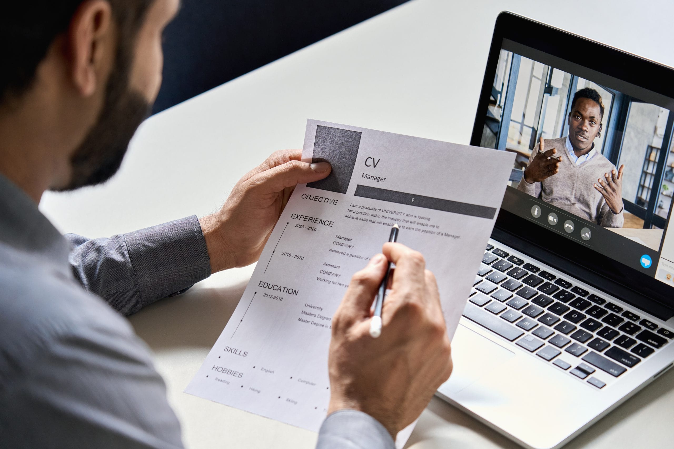 A hiring manager looks at a CV while conducting a video interview on a laptop
