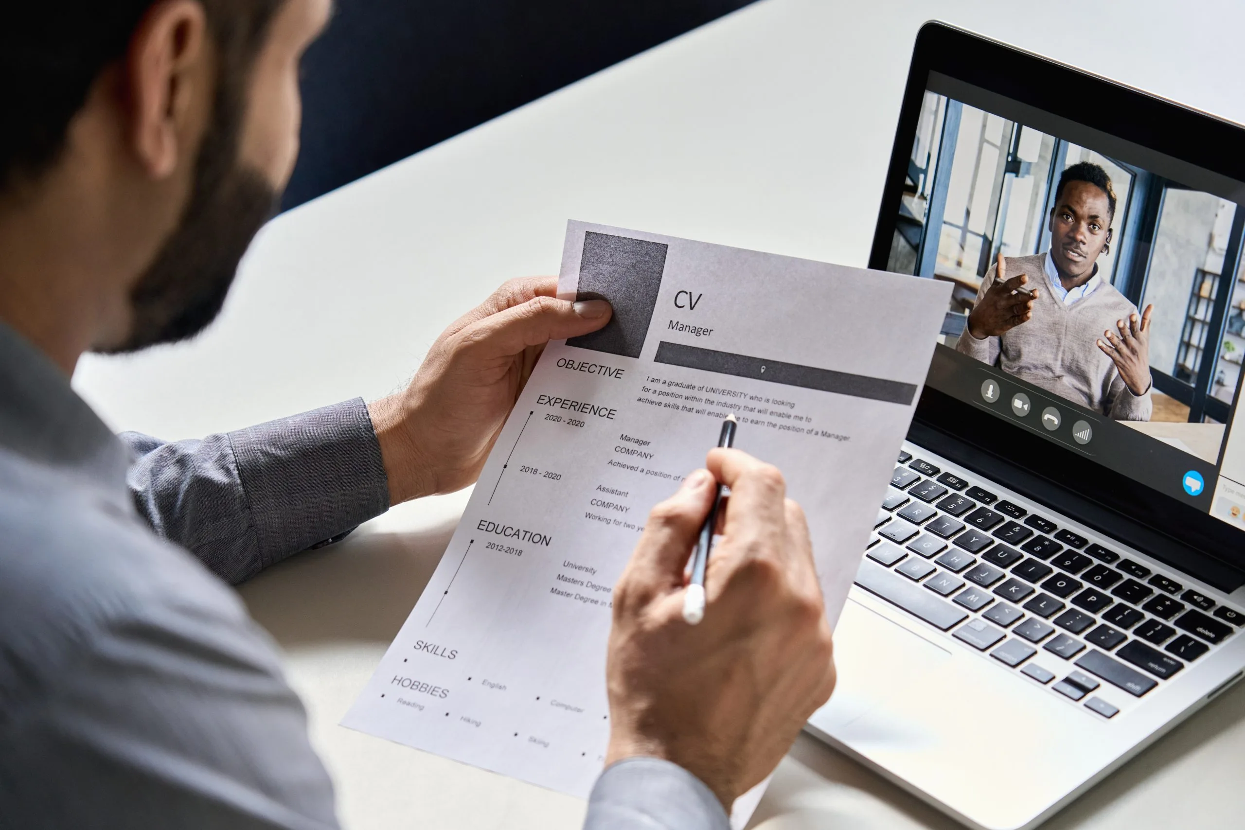 A hiring manager looks at a CV while conducting a video interview on a laptop